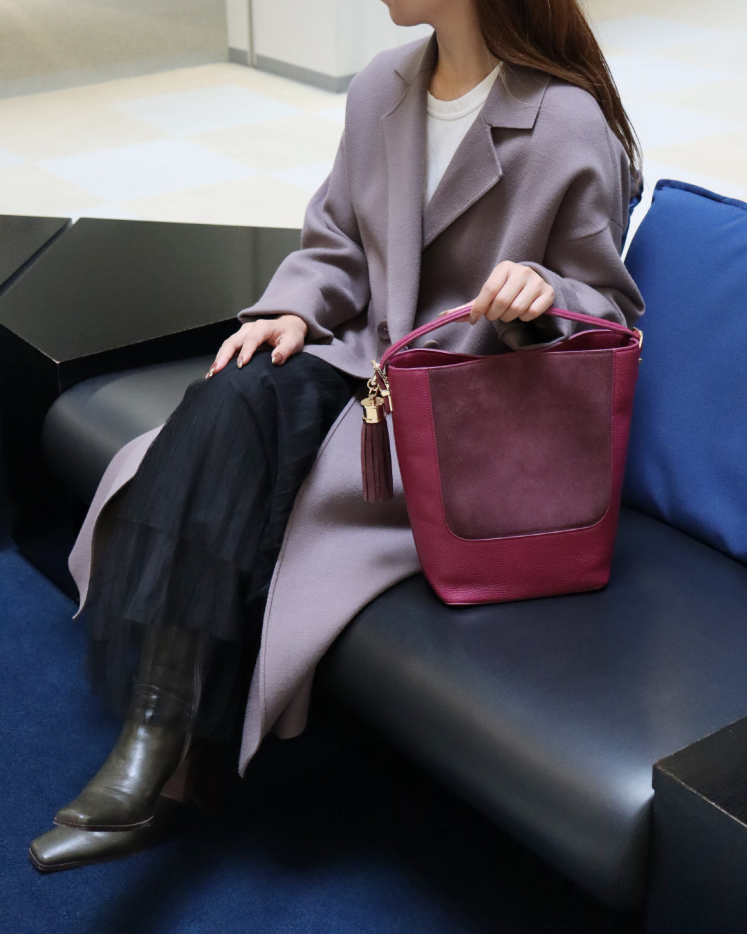 椅子に座った女性がワイン色のバッグに左手を添えている画像。