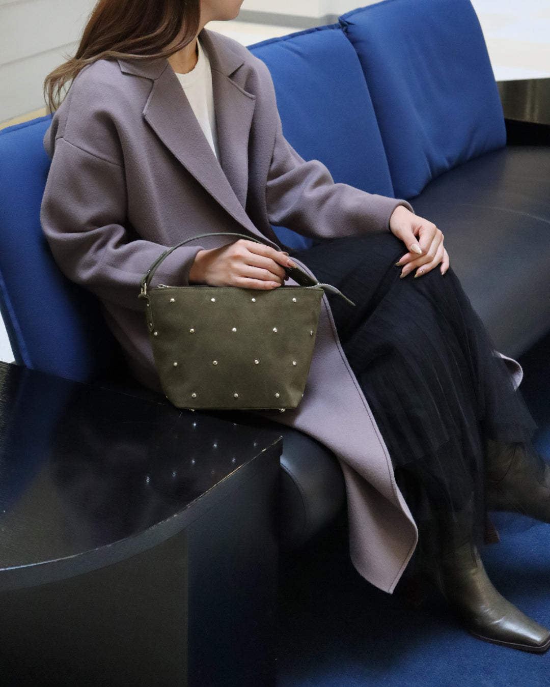 椅子に座っている女性がカーキ色のバッグに右手を掛けている画像。