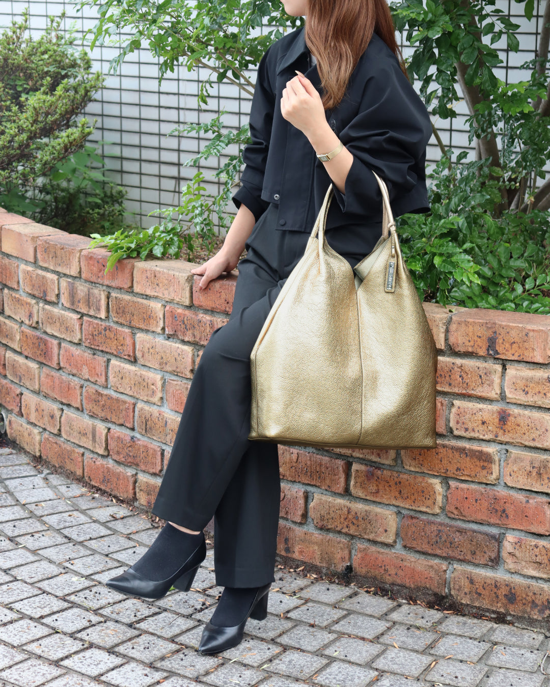 女性が左肘にコールド色のバッグを掛けて座っている画像。